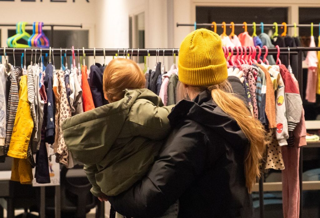 A parent and child looking through racks of children's clothes.